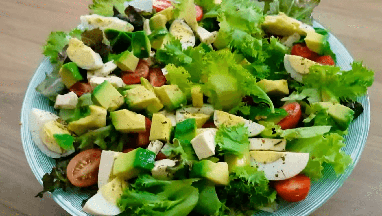 Fresh avocado salad with mixed greens, cherry tomatoes, boiled eggs, cheese cubes, and lemon olive oil dressing