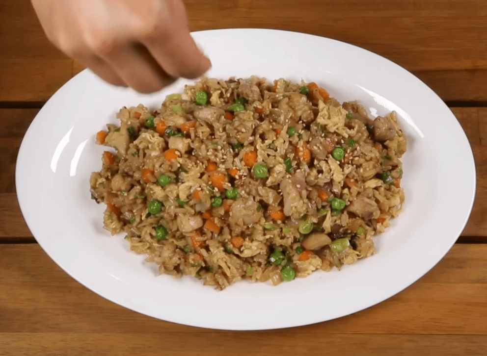 A close-up shot of a steaming bowl of Chicken Fried Rice featuring juicy golden-brown chicken thighs, scrambled eggs, bright green peas, and diced carrots, garnished with fresh green onions and sesame seeds.