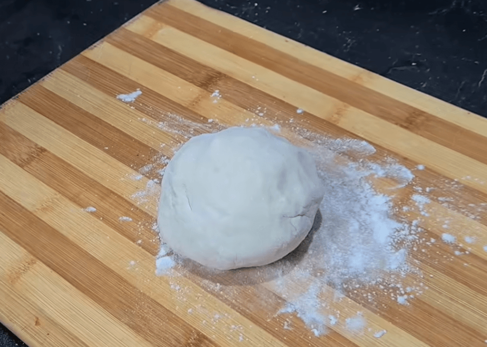 A golden brown thin crust pizza with turkey and mozzarella made using a homemade Brazilian pizza dough recipe on a floured surface.
