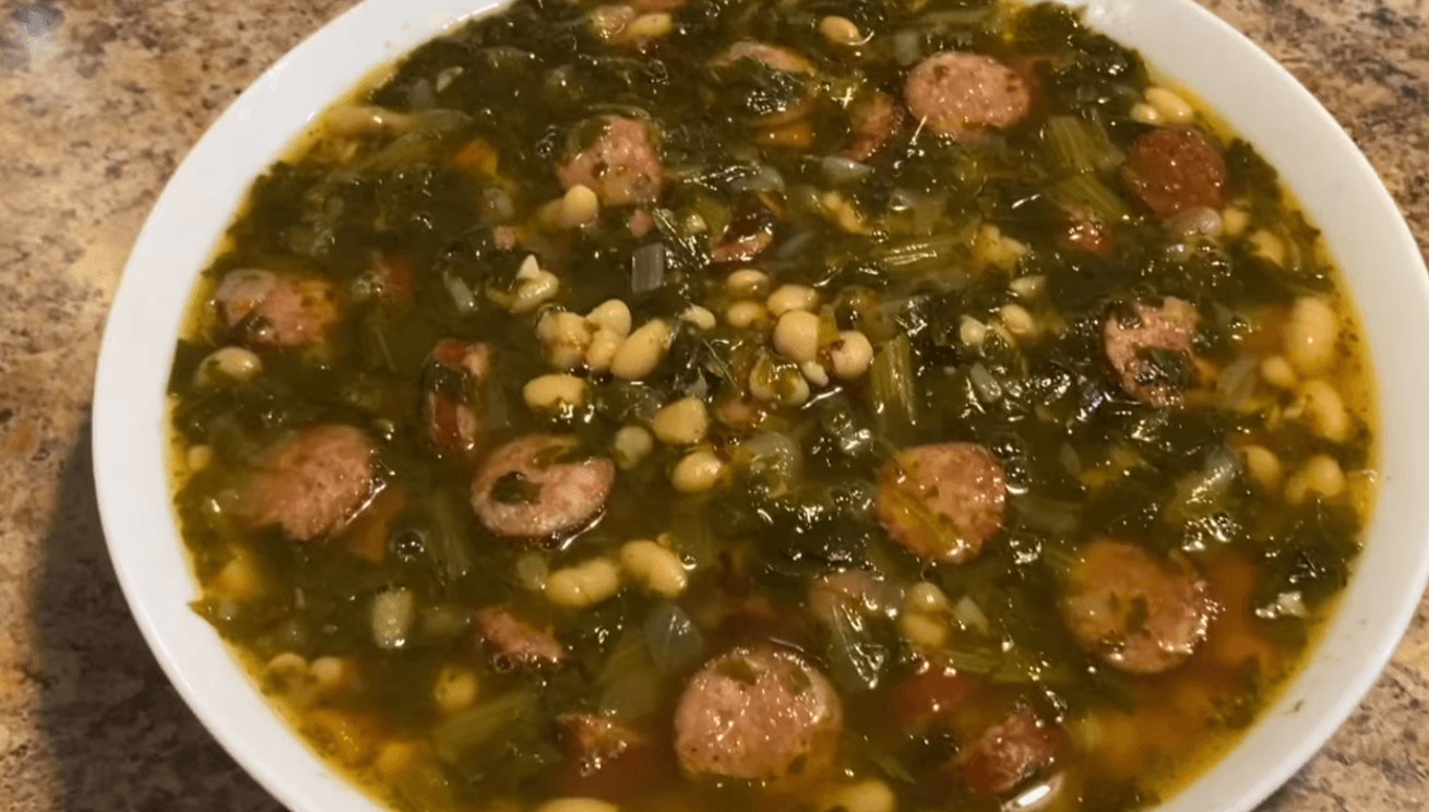 A steaming bowl of Southern Swamp Soup featuring rich broth, turnip greens, sliced smoked sausage, and white beans, served with a side of fresh cornbread.
