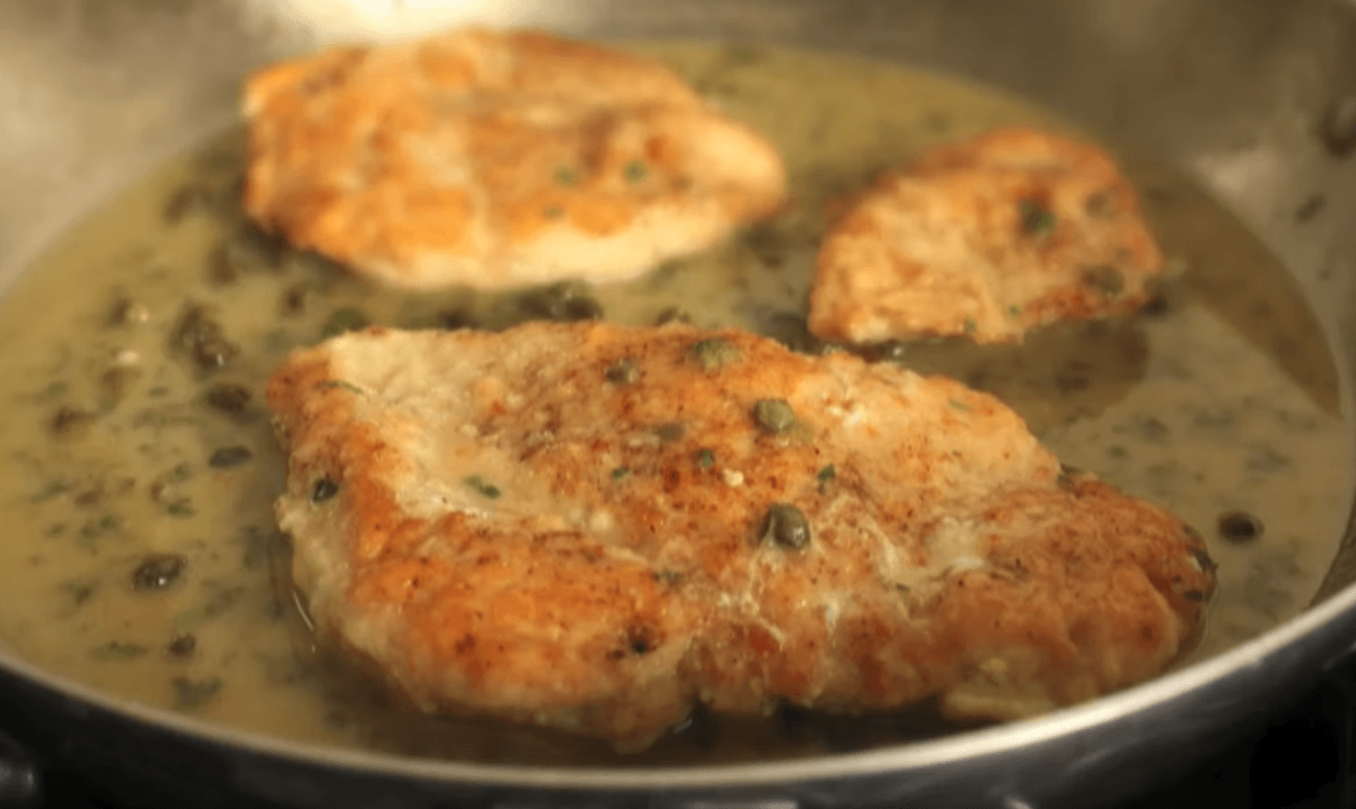 A heavy skillet filled with an easy chicken piccata recipe, featuring two golden-brown chicken breasts smothered in a glossy lemon caper sauce and garnished with fresh parsley.