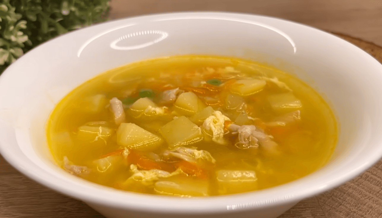 A steaming white bowl of Grandma’s homemade chicken soup recipe with visible carrots, peas, and tender chicken pieces on a rustic wooden table.