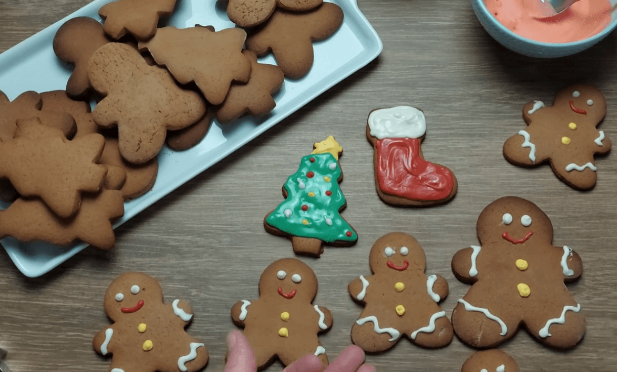 A close-up overhead shot of freshly baked homemade gingerbread cookies shaped like little people, beautifully decorated with colorful white chocolate details.