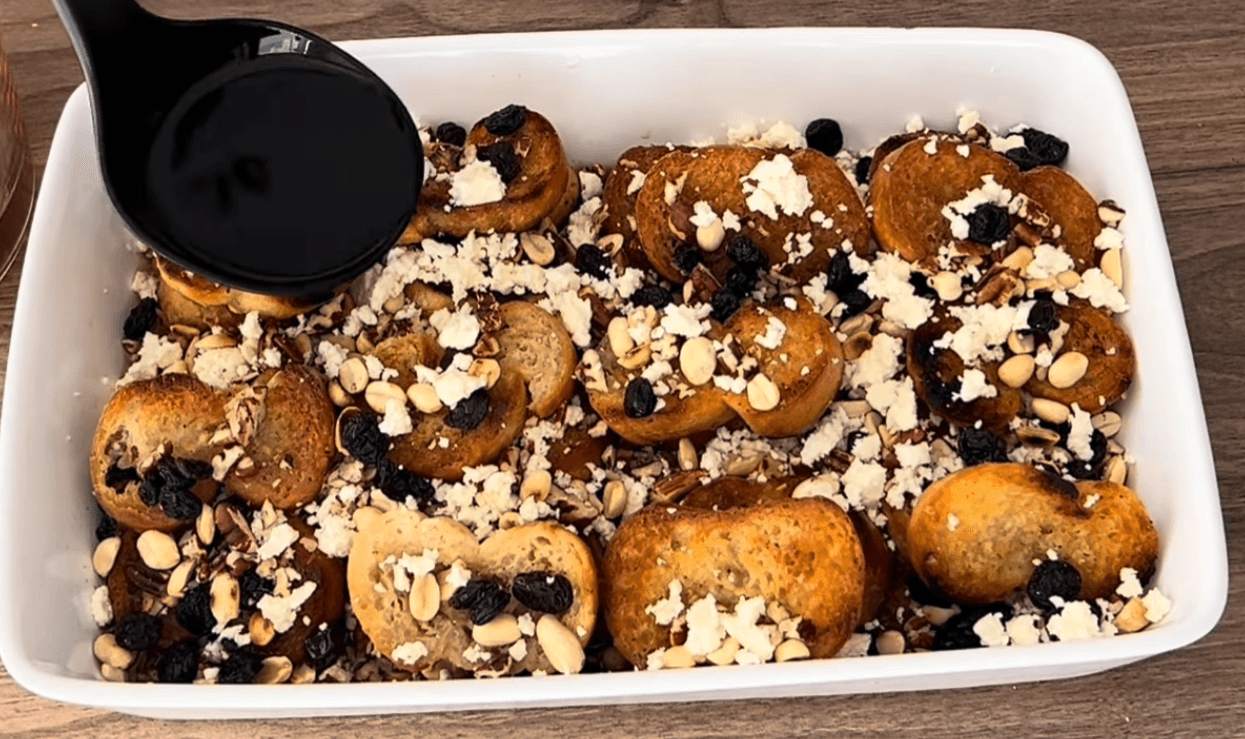 A close-up view of a traditional capirotada recipe, featuring warm, spiced bread pudding topped with toasted peanuts, raisins, and crumbled white cheese.